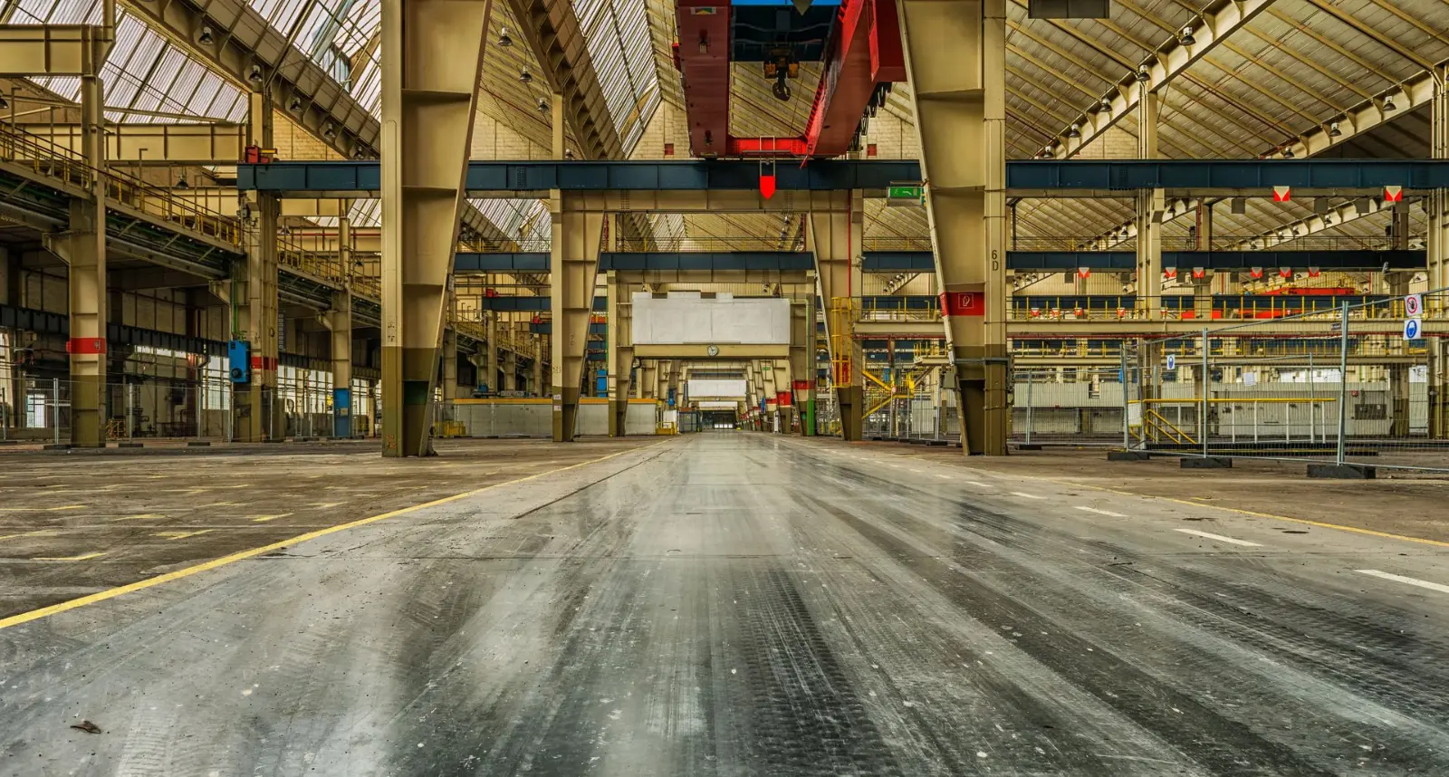 Vaste hall industriel de grande hauteur, charpente métallique et ponts roulants au-dessus d’un plateau vide